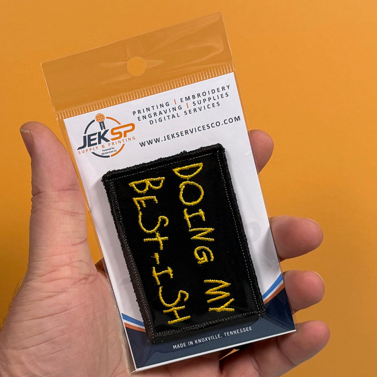 Doing My Best-ish patch in black with yellow handwritten lettering, retail package held in a hand