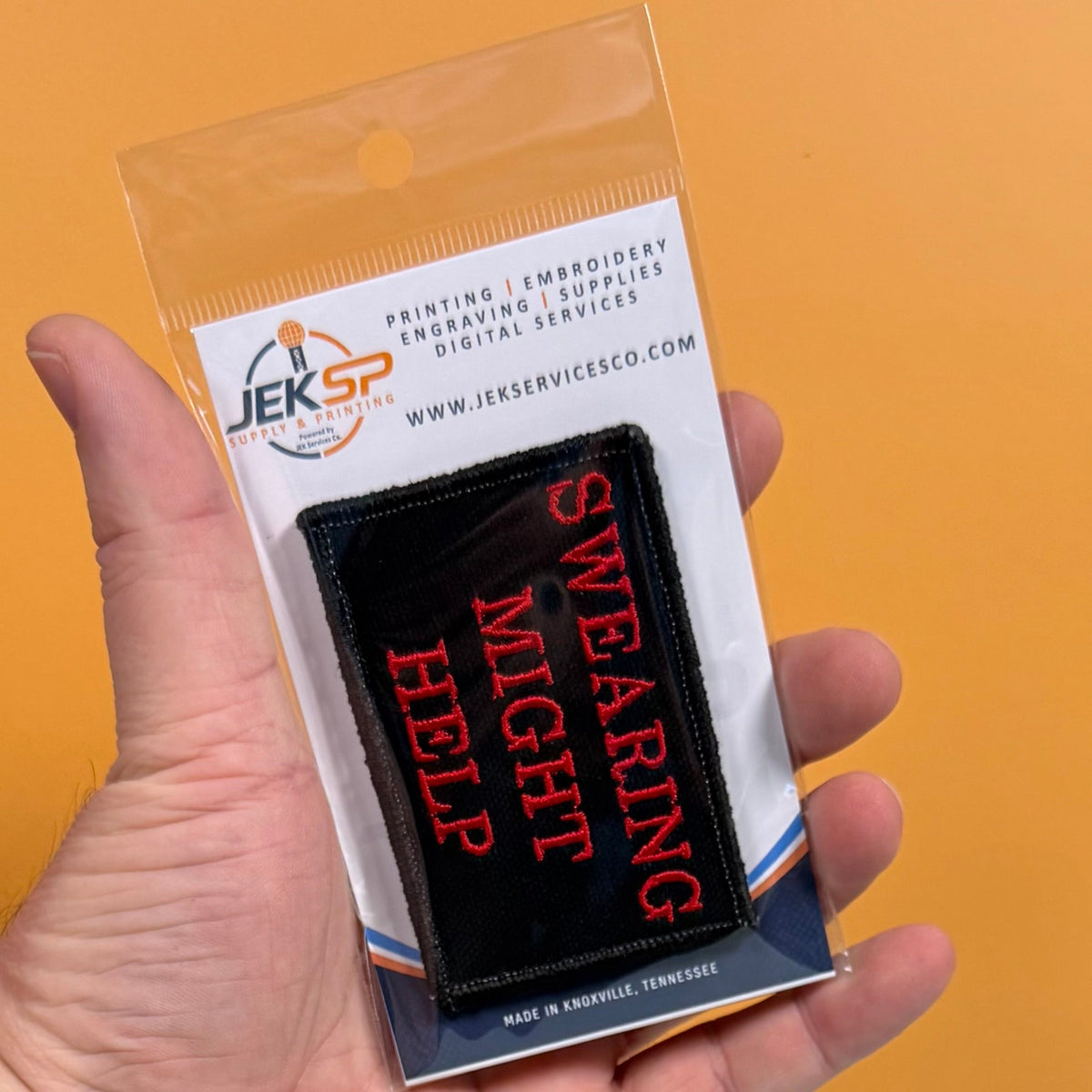 Swearing Might Help patch in black with red lettering, retail package held in a hand