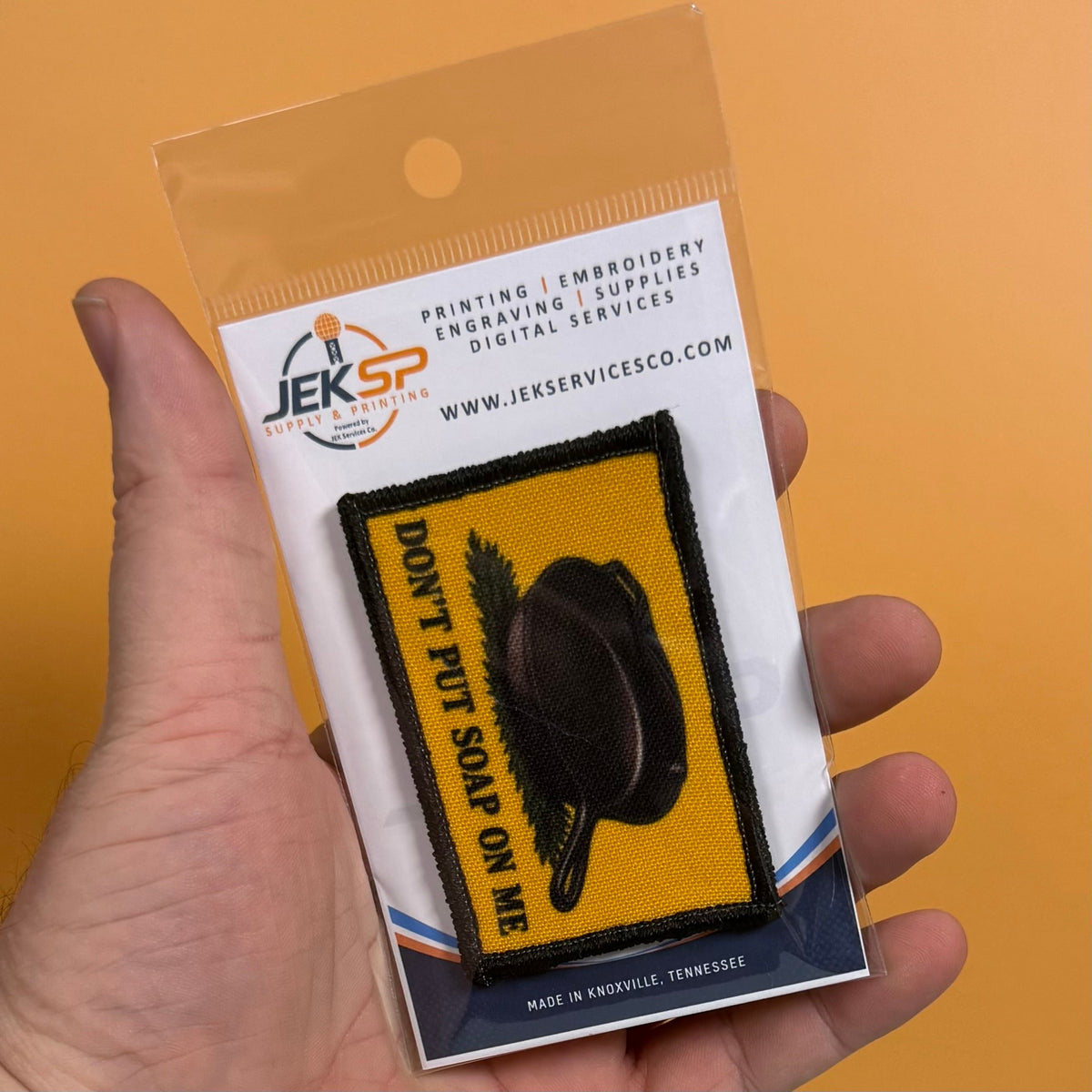 Iron Skillet Gadsden, Don't Put Soap On Me patch in yellow with a black skillet silhouette and lettering, retail package held in a hand