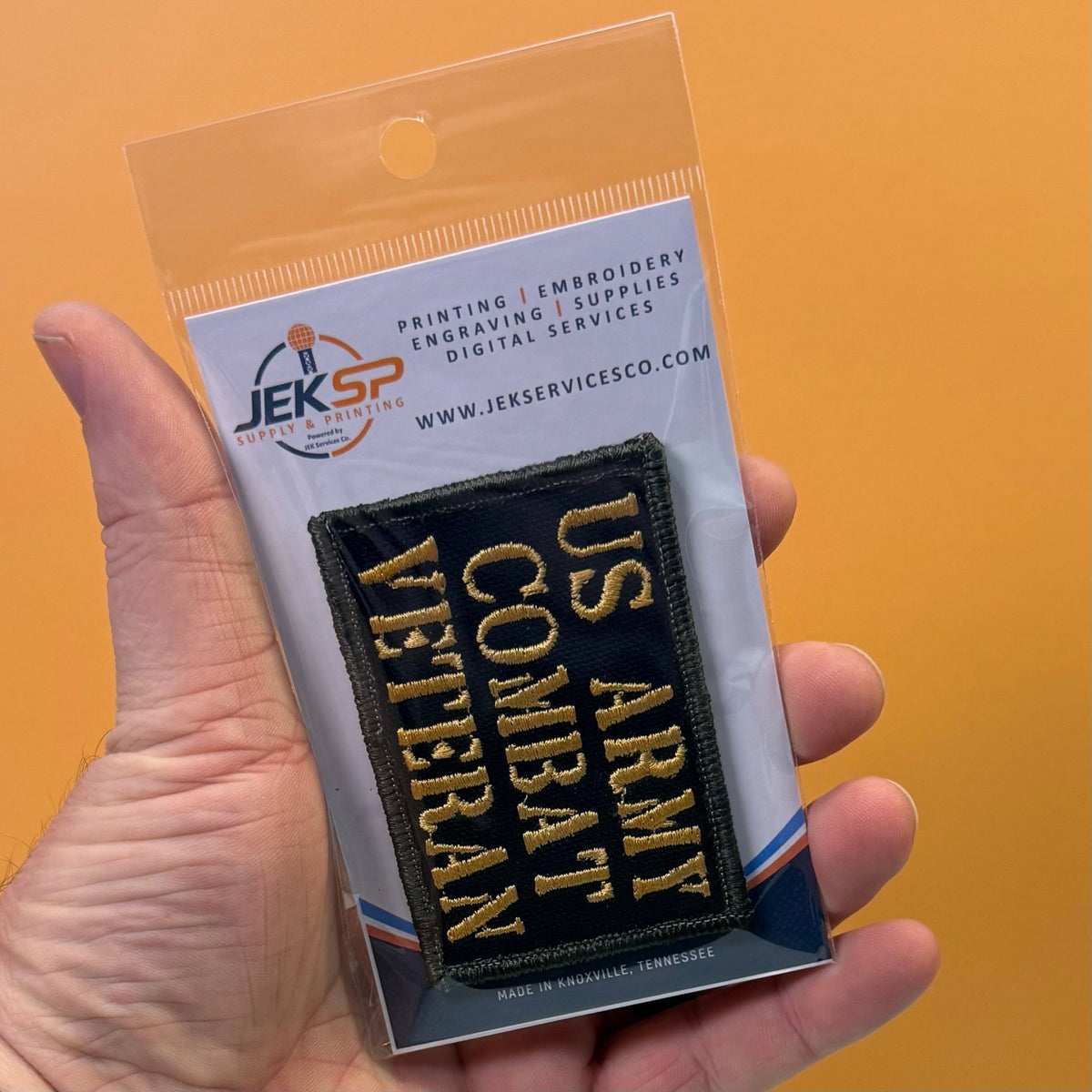 US Army Combat Veteran patch in black with tan lettering, retail package held in a hand