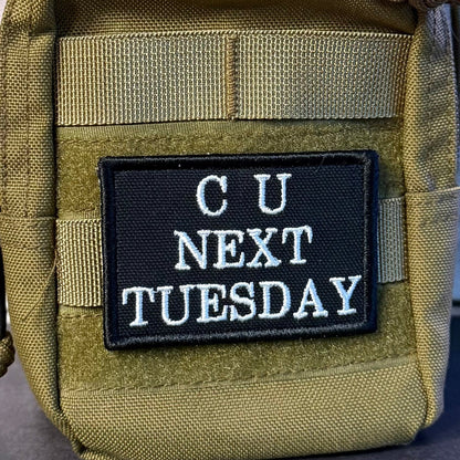 See You Next Tuesday patch in black with white C U NEXT TUESDAY lettering, mounted on an olive backpack