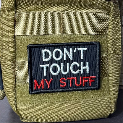 Don't Touch My Stuff patch in black with white and red lettering, mounted on an olive backpack