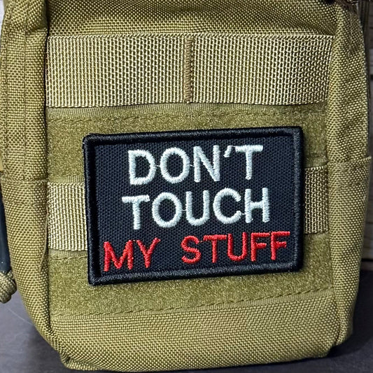 Don't Touch My Stuff patch in black with white and red lettering, mounted on an olive backpack
