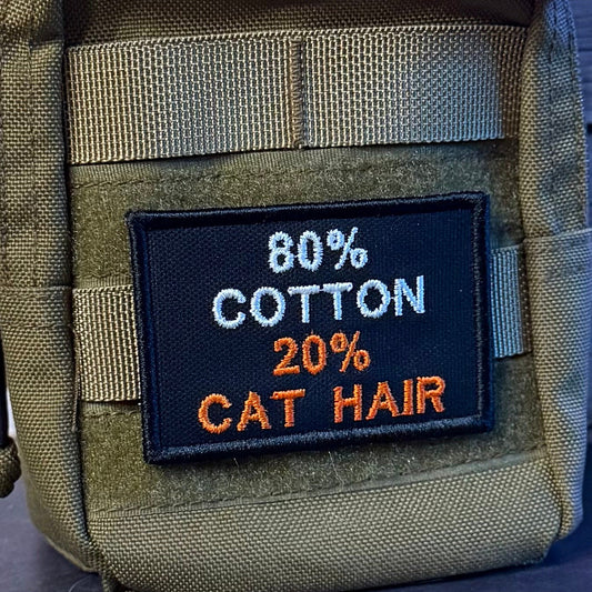 80% Cotton 20% Cat Hair patch in black with white 80% COTTON and orange 20% CAT HAIR lettering, mounted on an olive backpack