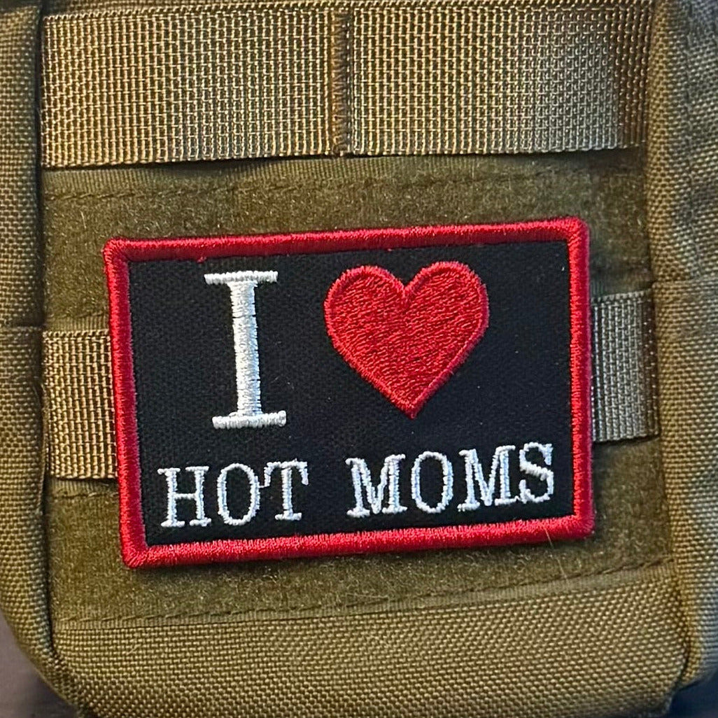 I Love Hot Moms MILFS patch in black with a red heart and border and white lettering, mounted on an olive backpack