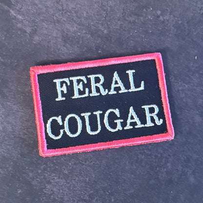 Front view of Feral Cougar patch in black with white lettering and pink border