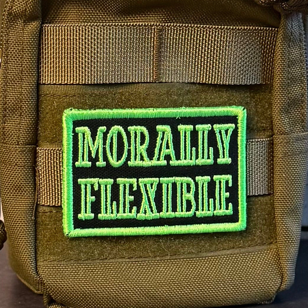 Morally Flexible patch in black with bright green lettering and border, mounted on an olive backpack