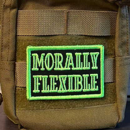 Morally Flexible patch in black with bright green lettering and border, mounted on an olive backpack