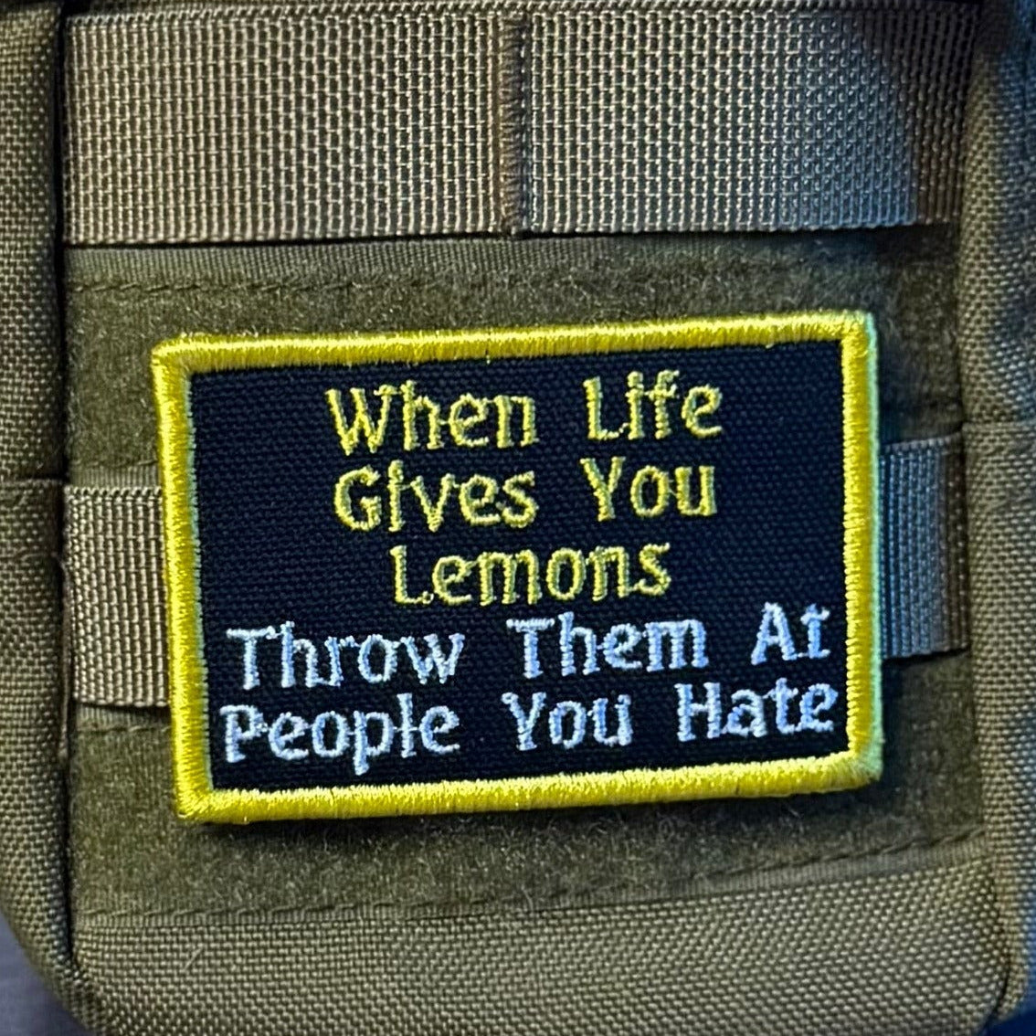 Throw Lemons At People You Hate patch in black with yellow and white lettering and a yellow border, mounted on an olive backpack
