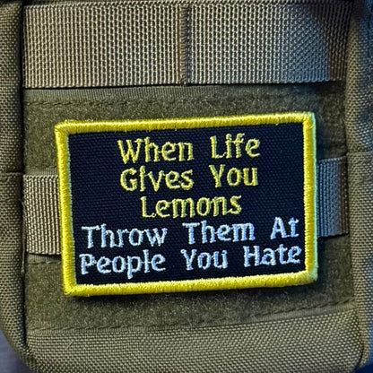 Throw Lemons At People You Hate patch in black with yellow and white lettering and a yellow border, mounted on an olive backpack