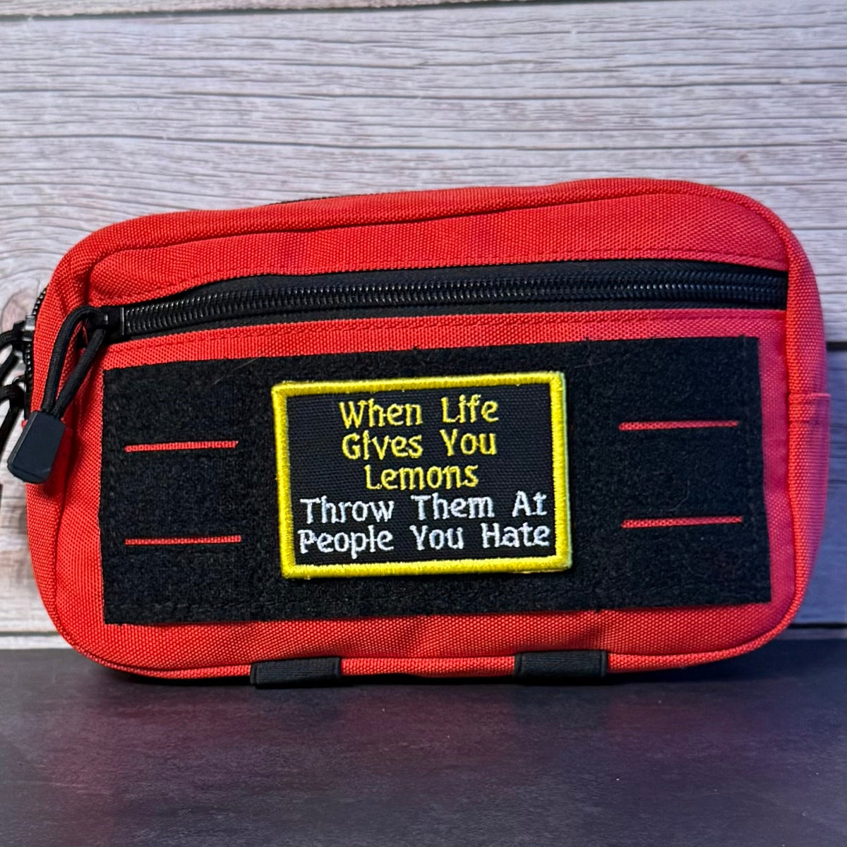 Throw Lemons At People You Hate patch in black with yellow and white lettering and a yellow border, mounted on a red utility pouch