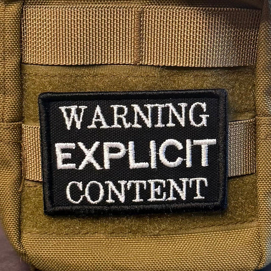 Explicit Content Warning patch in black with white lettering, mounted on an olive backpack