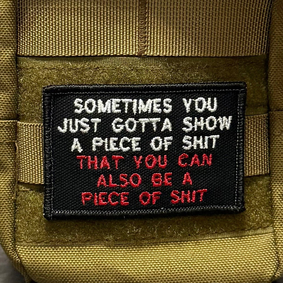 Sometimes You Just Gotta Show a Piece of Shit patch in black with white and red lettering, mounted on an olive backpack