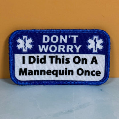 Front view of Don’t Worry I Did This On A Mannequin Once patch in blue and white with black lettering and medical symbols