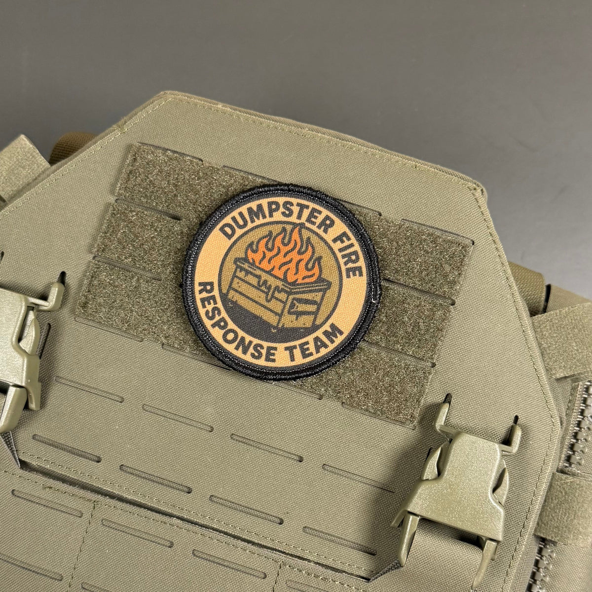 Dumpster Fire Response Team patch in tan and black with an orange flaming dumpster, mounted on a tan plate carrier
