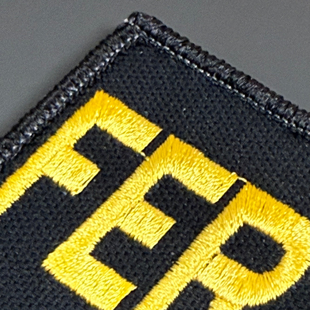 Feral & Wild patch in black with yellow FERAL lettering, close-up of embroidery