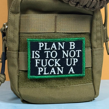 Plan B, Don't Fuck Up Plan A patch in black with white lettering and a green border, mounted on an olive backpack