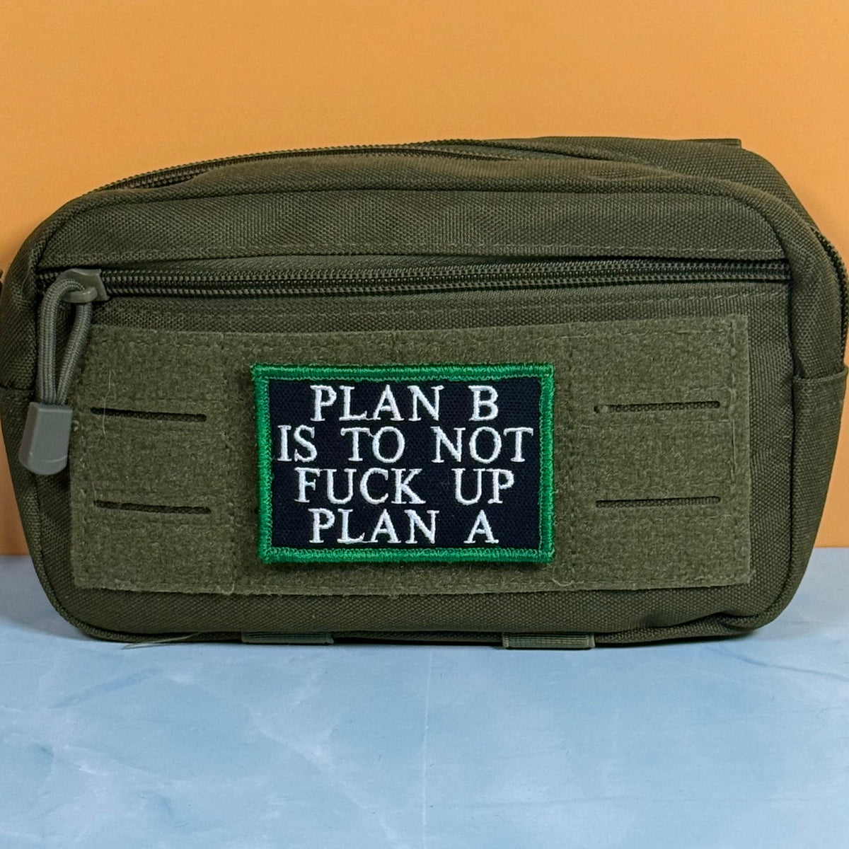 Plan B, Don't Fuck Up Plan A patch in black with white lettering and a green border, mounted on an olive utility pouch