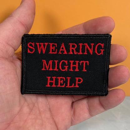 Swearing Might Help patch in black with red lettering, held in a hand