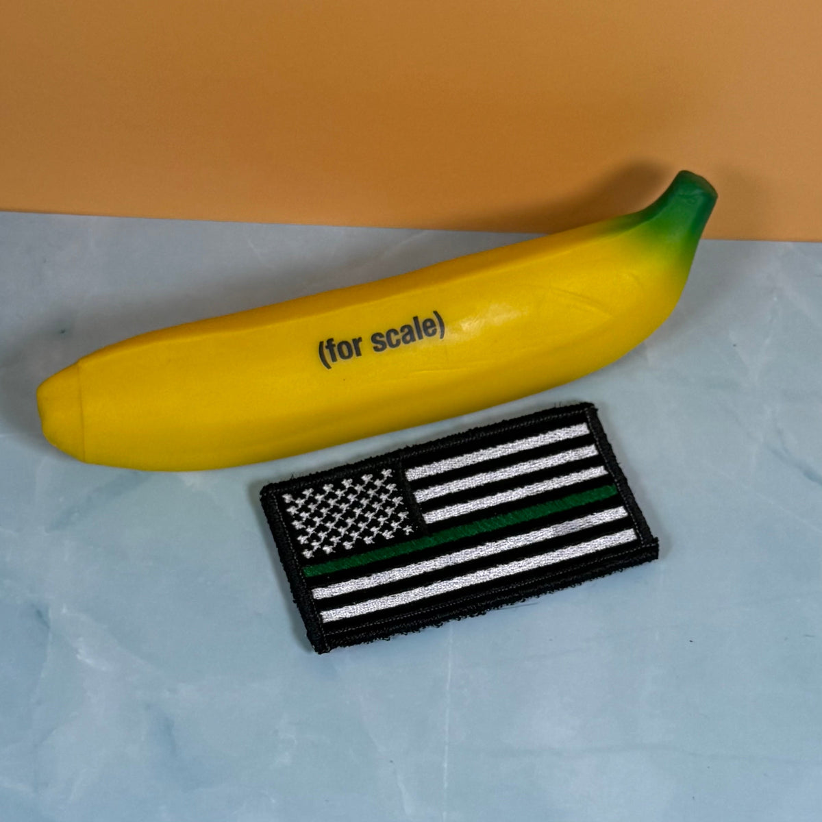 Thin Green Line Tactical American Flag patch in black and white American flag with one green stripe, beside a yellow banana-shaped object