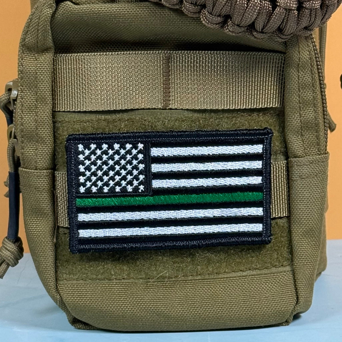 Thin Green Line Tactical American Flag patch in black and white American flag with one green stripe, mounted on an olive backpack