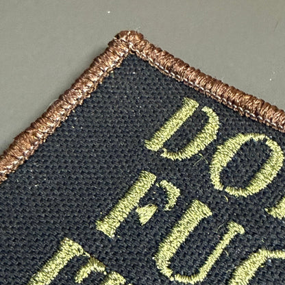 Don't Fuck It Up patch in black with olive-green lettering and a tan border, close-up of embroidery