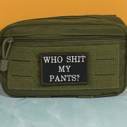 Who Shit My Pants? patch in black with white lettering and a brown border, mounted on an olive utility pouch