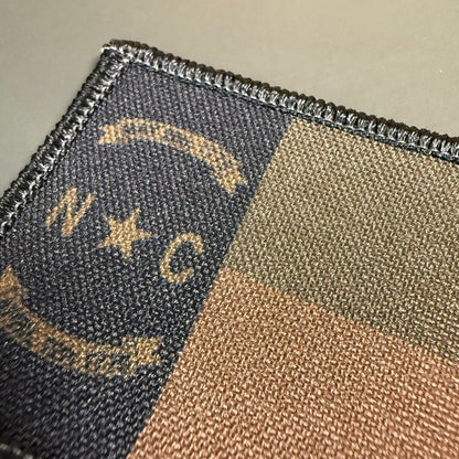 North Carolina State Flag patch in subdued tan and dark blue North Carolina flag with N C lettering and star, close-up of embroidery