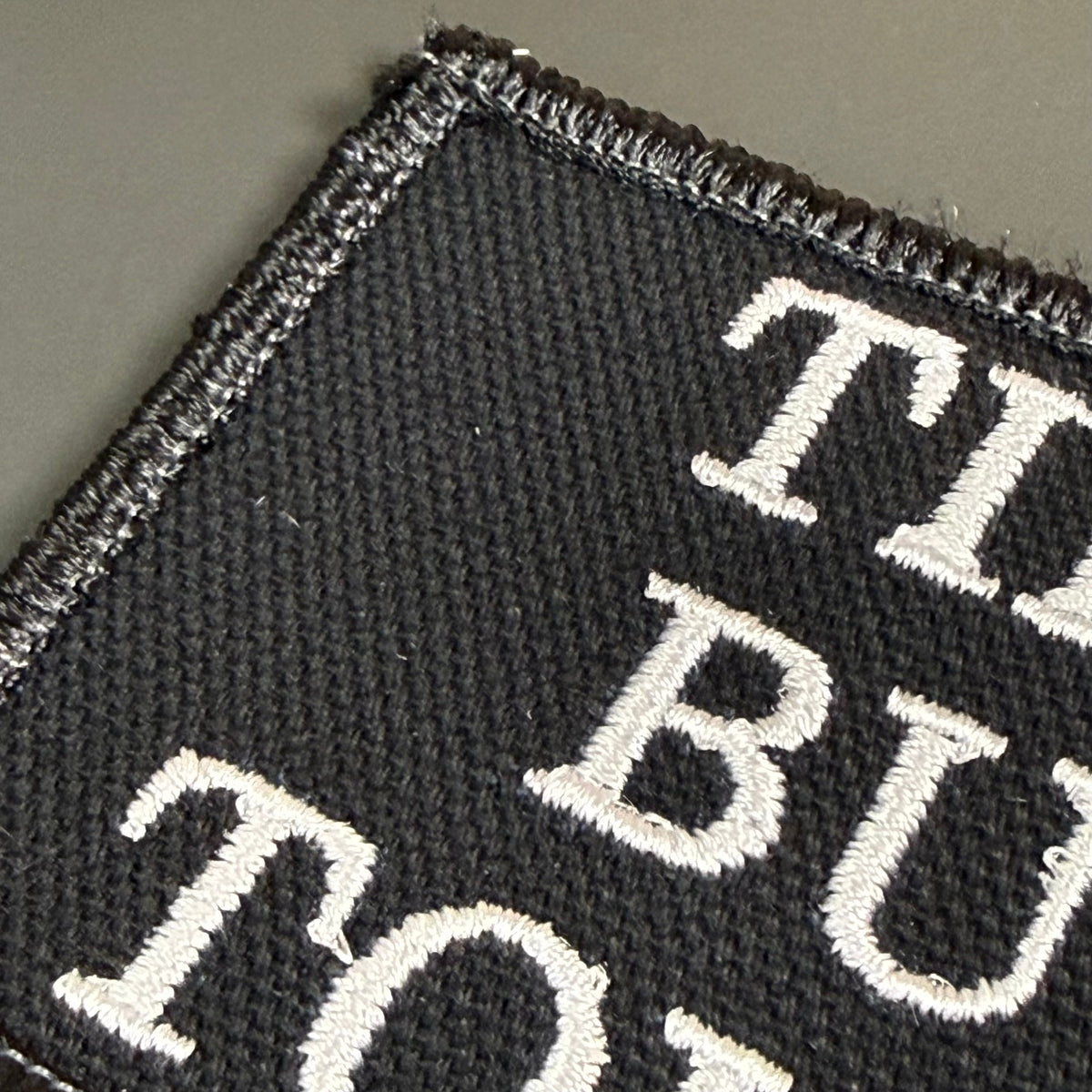 Tiny But Tough patch in black with white lettering, close-up of embroidery