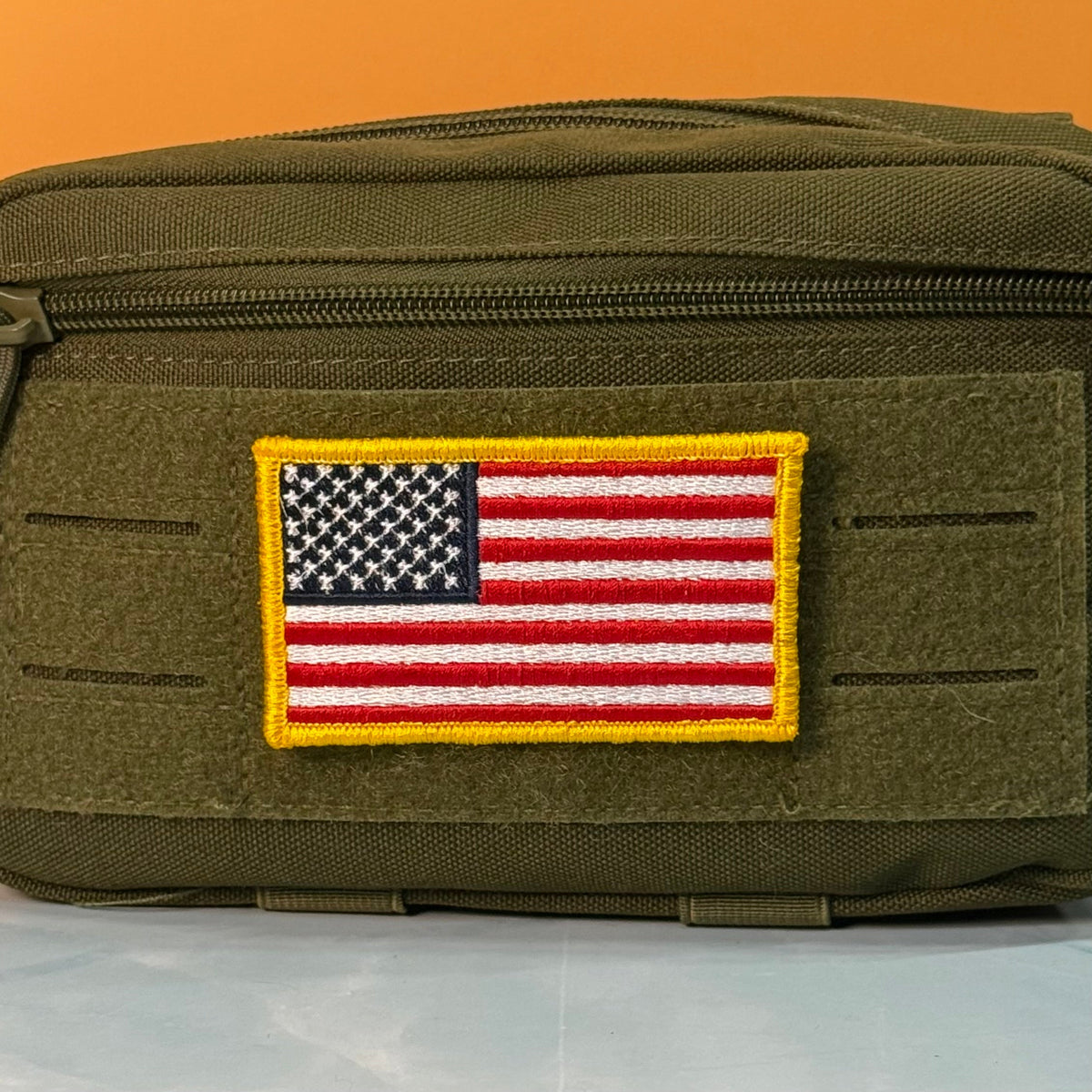 American Flag patch in red, white and blue stars and stripes with a yellow border, mounted on an olive utility pouch