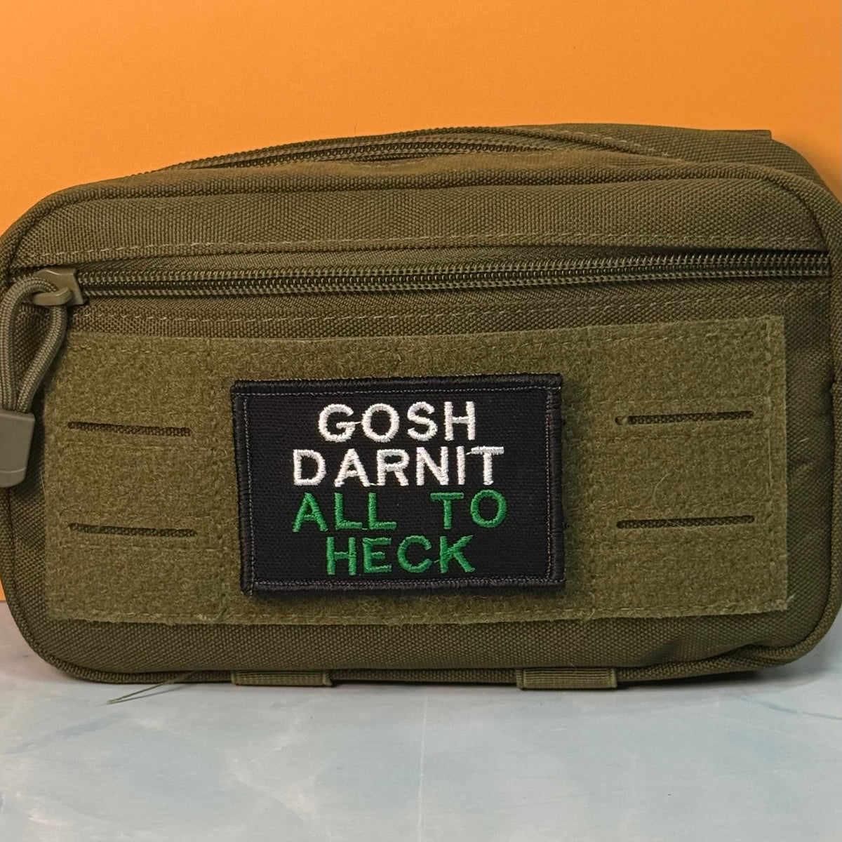 Gosh Darnit All To Heck, Polite Swearing patch in black with white and green lettering, mounted on an olive utility pouch