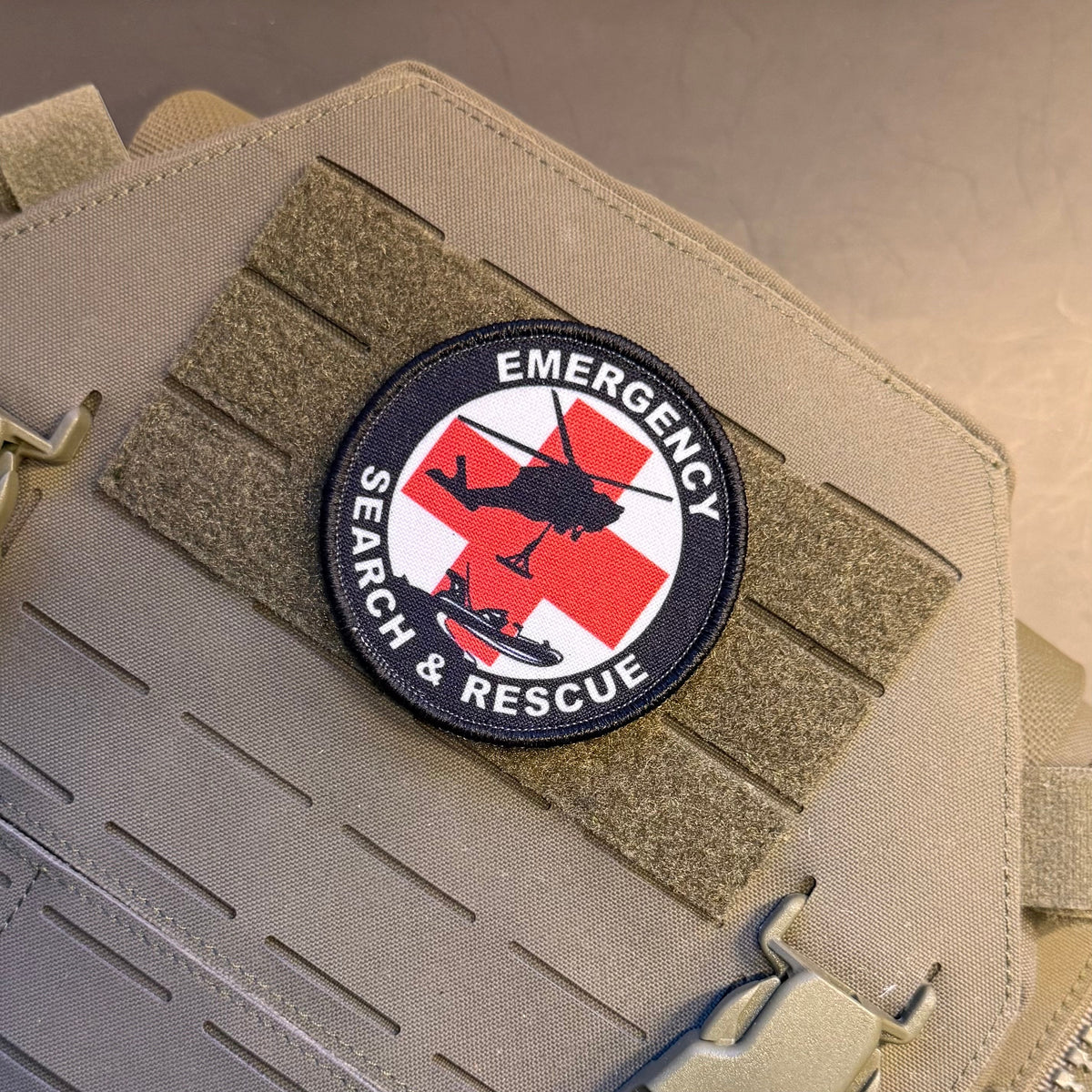 Round Emergency Search and Rescue printed patch with a red cross and black aircraft silhouettes, mounted on a tan plate carrier
