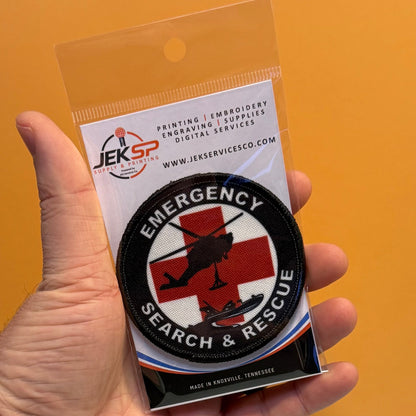 Round Emergency Search and Rescue printed patch with a red cross and black aircraft silhouettes, in retail packaging held in a hand
