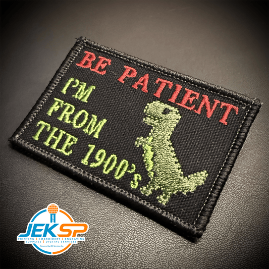 Front view of Be Patient I'm From The 1900's patch in black with red and green lettering and a green dinosaur
