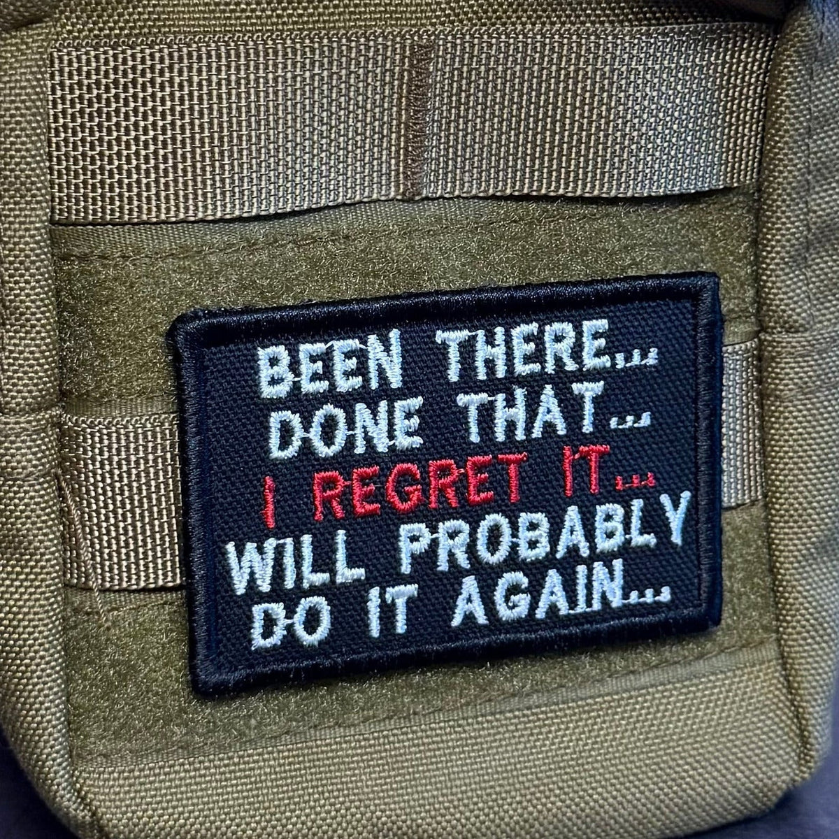 Been There, Done That, I Regret It, Will Probably Do It Again patch in black with white and red lettering, mounted on an olive backpack