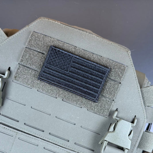 Blackout No Quarters Given American Flag patch in all-black American flag, mounted on a tan plate carrier