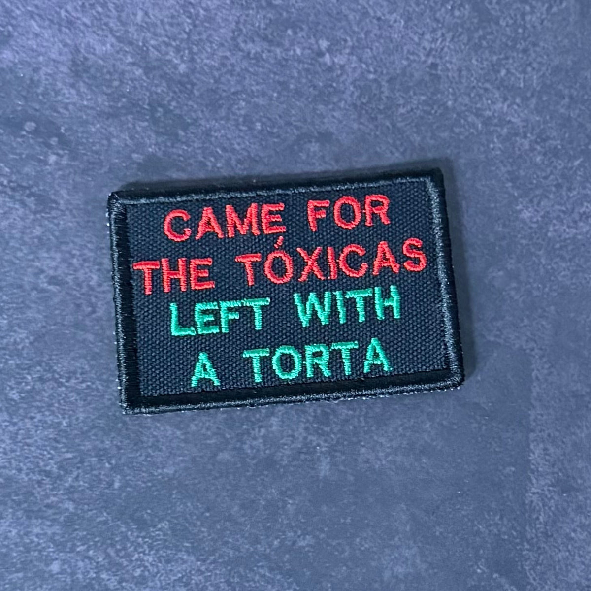 Front view of Came For The Toxicas, Left With A Torta patch in black with red and green lettering