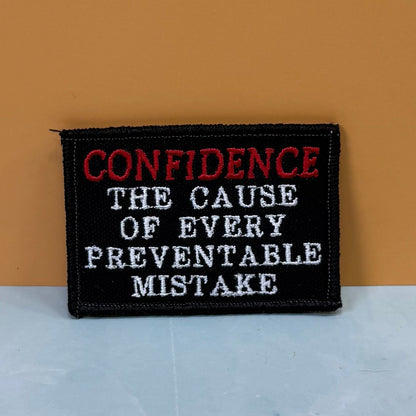 Front view of Confidence Causes Mistakes patch in black with red CONFIDENCE and white lettering
