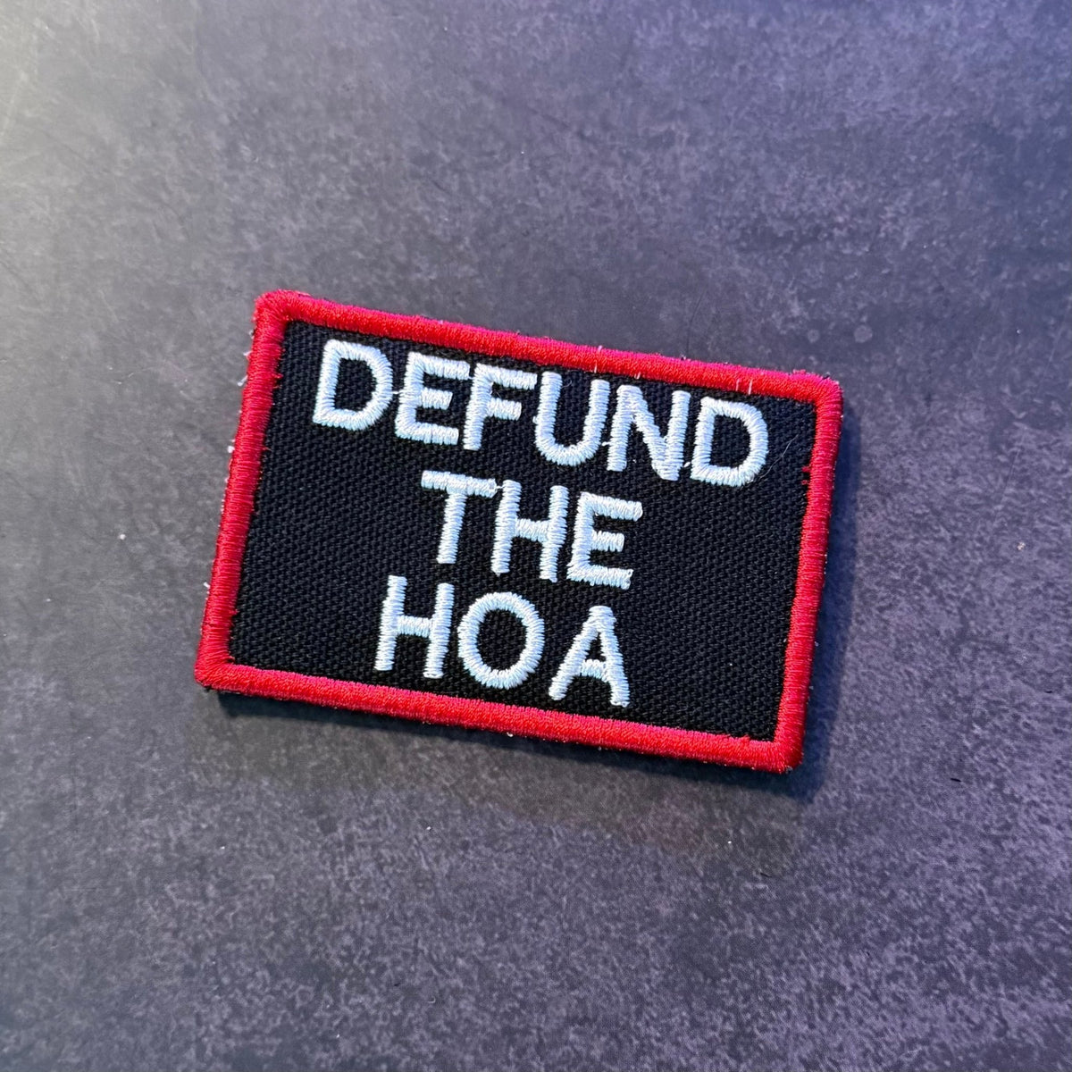 Front view of Defund the HOA patch in black with white lettering and a red border