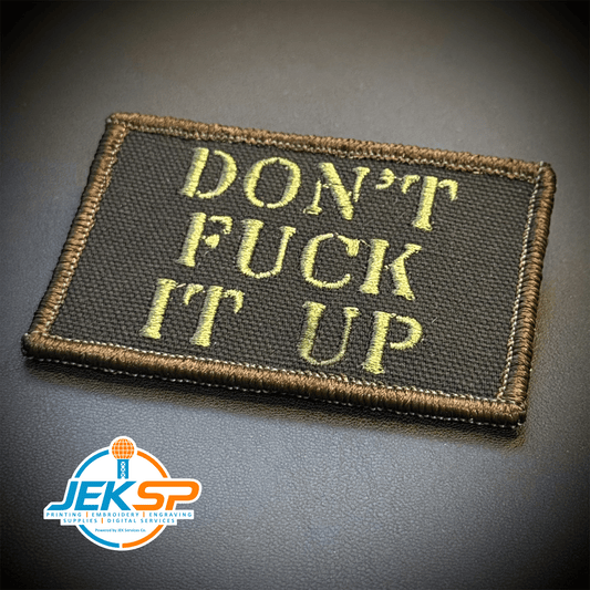 Front view of Don't Fuck It Up patch in black with olive-green lettering and a tan border
