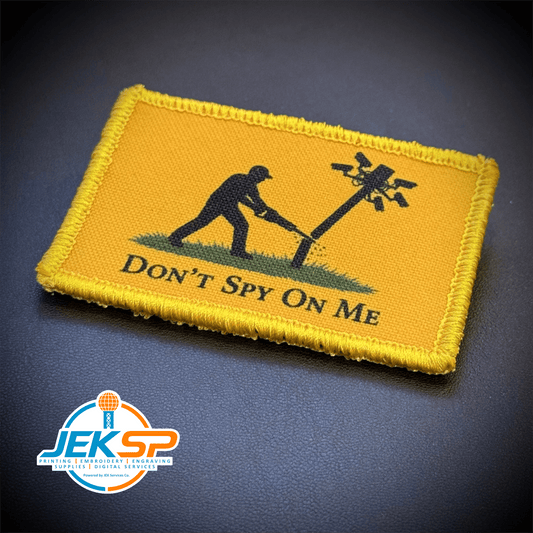 Front view of Don't Spy On Me, Anti-Flock Cameras patch in yellow with a black figure kicking a camera pole and black lettering