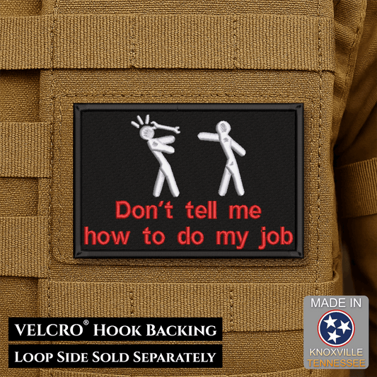 Front design and hook backing of Don't Tell Me How To Do My Job patch in black with two white figures and red lettering