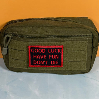 Good Luck, Have Fun, Don't Die patch in black with red lettering and border, mounted on an olive utility pouch