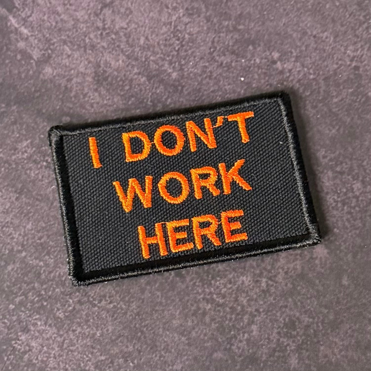 Front view of I Don't Work Here patch in black with orange lettering
