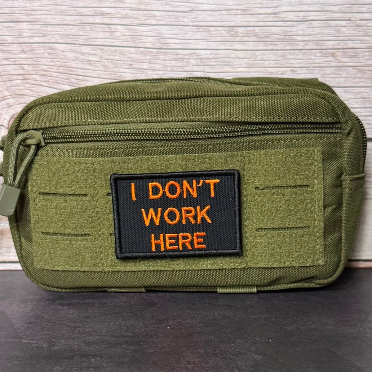 I Don't Work Here patch in black with orange lettering, mounted on an olive utility pouch