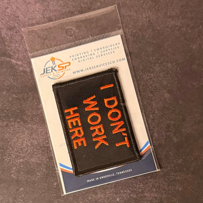 I Don't Work Here patch in black with orange lettering, in clear retail packaging