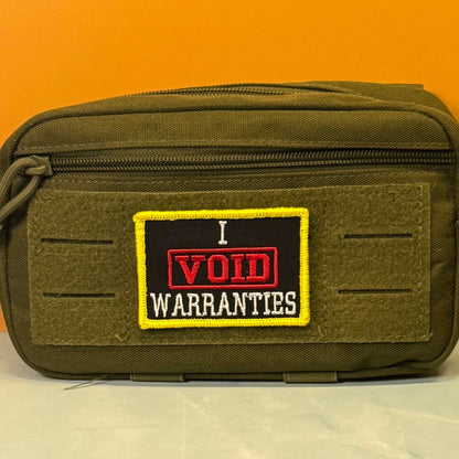 I Void Warranties patch in black with a red VOID stamp, white lettering and yellow border, mounted on an olive utility pouch