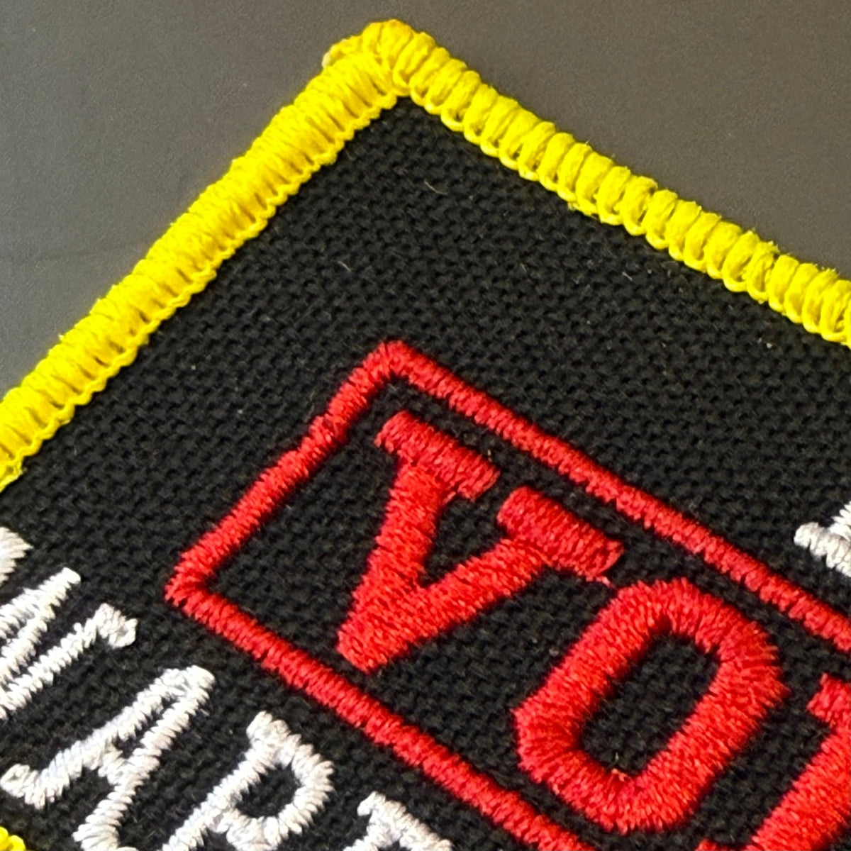 I Void Warranties patch in black with a red VOID stamp, white lettering and yellow border, close-up of embroidery