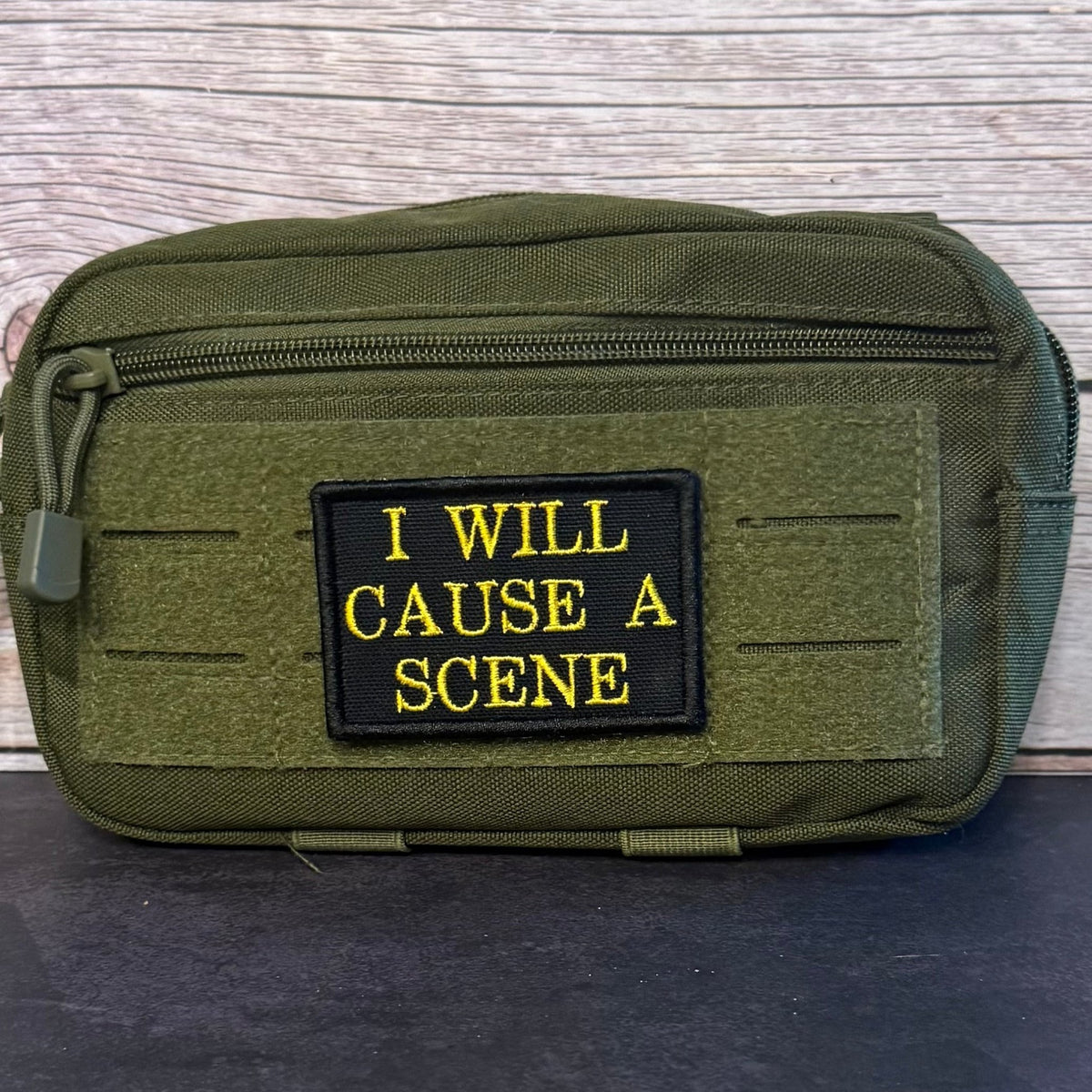 I Will Cause A Scene patch in black with yellow lettering, mounted on an olive utility pouch