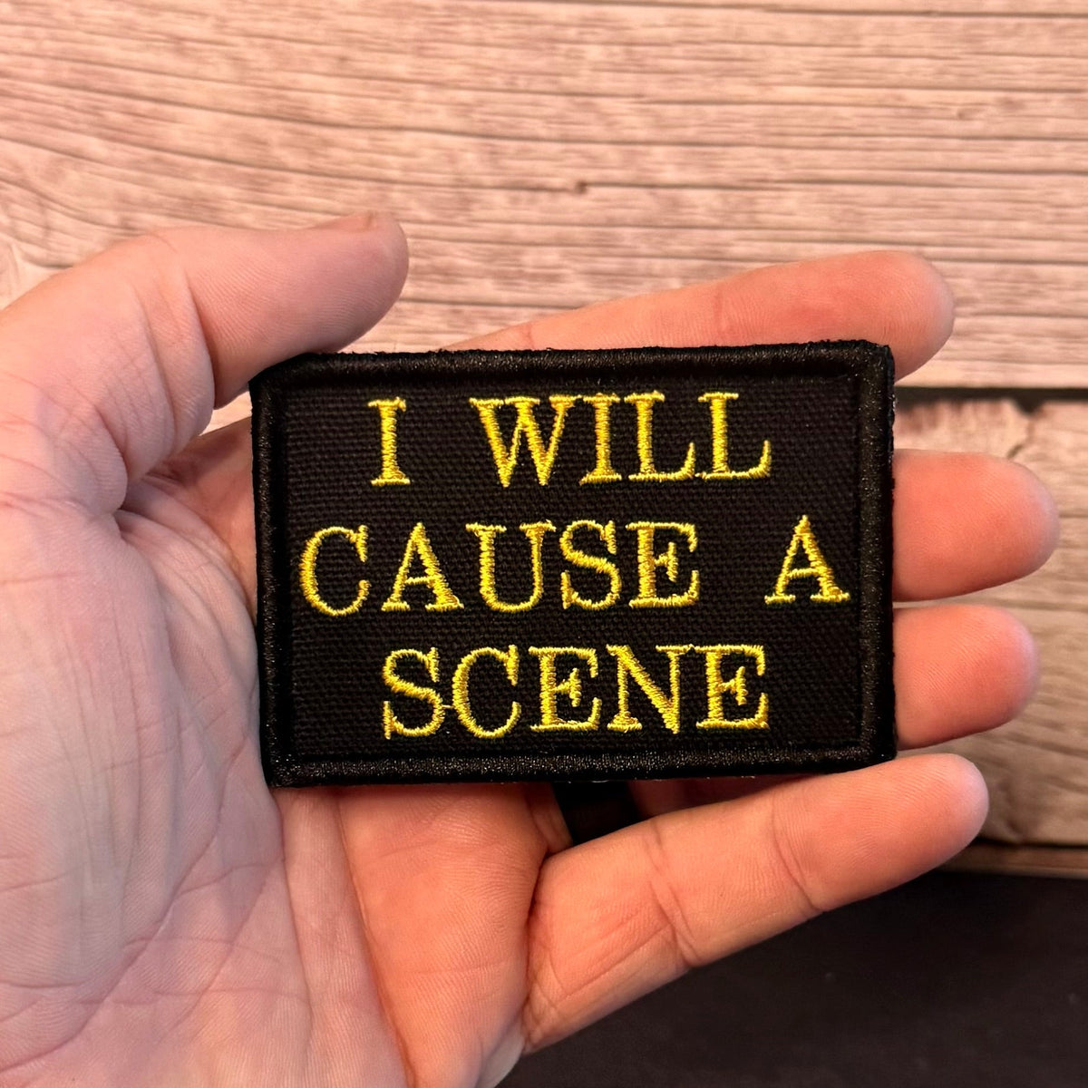 I Will Cause A Scene patch in black with yellow lettering, held in a hand